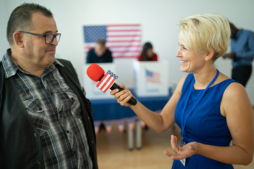 A man is standing in front of a microphone held by a reporter while standing in an election center
