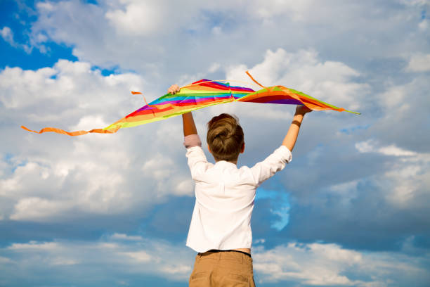 istock A handsome boy in a white shirt with a multicolored kite on a blue sky background 1421927338