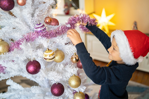 A smiling boy reaching up to hang the tinsel around the Christmas Tree