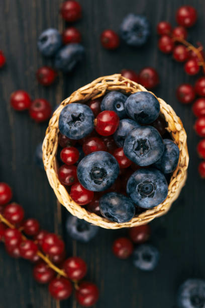 istock Berries in a wicker basket on a dark background: blueberries and red currants, top view. Summer fresh berries 1421933000