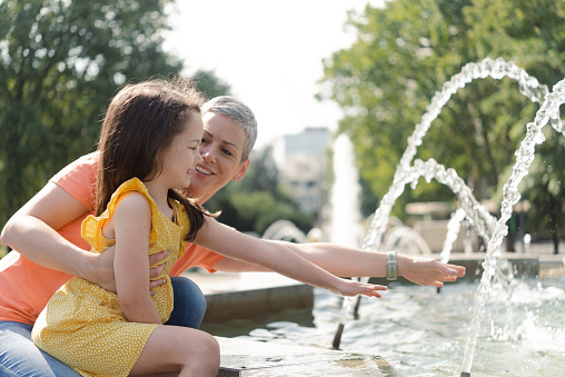 Portrait of a happy mother and her little daughter enjoying in the park by the fountain