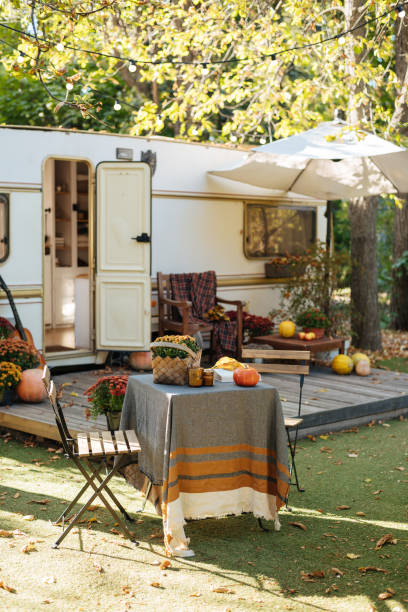 istock Caravan mobile home with terrace, Mobile home decorated with autumn decor. Cozy atmosphere - table and chairs, flowers, fallen leaves, pumpkins. Caravan camping. mobile home trailer. Selective focus 1421935367