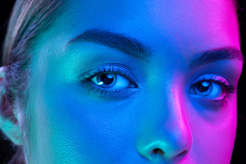 Blue eyes. Close up eyes of beautiful young girl looking camera in pink neon light. Concept of cosmetics, makeup, natural and eco treatment, skin care. Shiny and healthy look, fashion, vision. Details