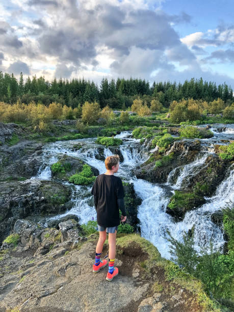Teenage boy with running shoes standing looking down on a waterfall Kermóafoss in Reykjavik Iceland stock photo