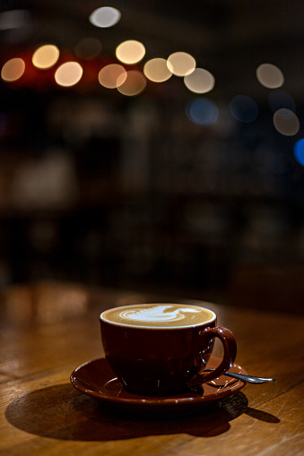 A cup of cappuccino latte art with bokeh lighting background in a cafe at night
