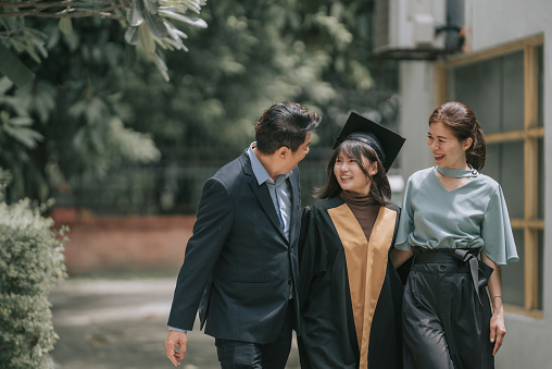 Proud Chinese parents walking together with daughter with graduation gowns in college