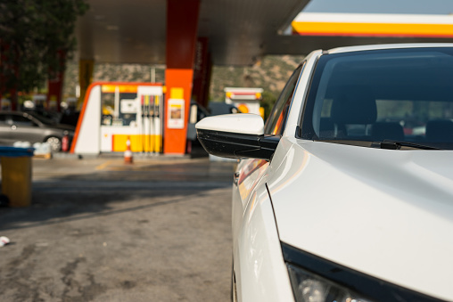 a white car is foreground gas station is background focus on foreground horizontal photo