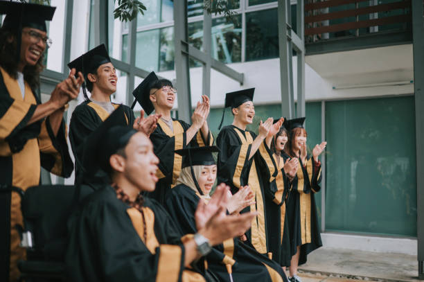 istock Asian diversify students in graduation gown clapping hands cheering for classmate during graduation ceremony outdoor 1421945318