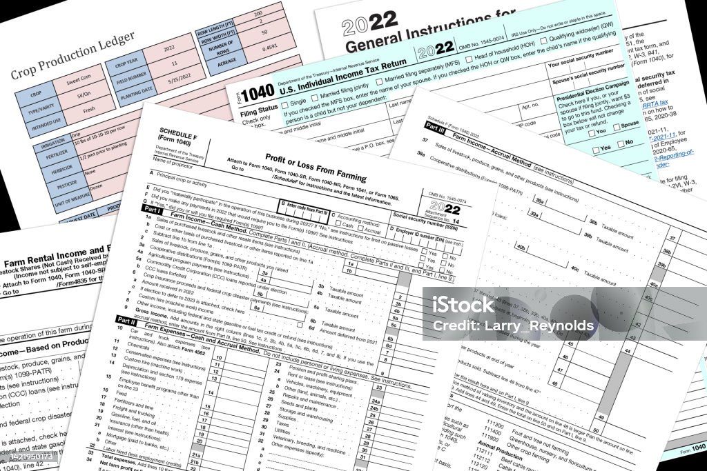 2022 IRS farming tax forms on a desk top. 2022 IRS 1040 & farm tax forms with a simulated crop production page on a black desktop. Tax Form Stock Photo
