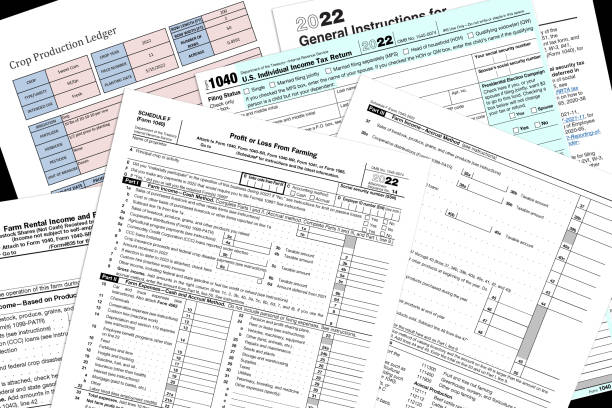 2022 IRS farming tax forms on a desk top. 2022 IRS 1040 & farm tax forms with a simulated crop production page on a black desktop. tax stock pictures, royalty-free photos & images