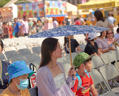 Toronto Ontario, Canada- September 2nd, 2022: An mom holding an umbrella while sitting with her two children during Toronto's Annual Dragon Festival.