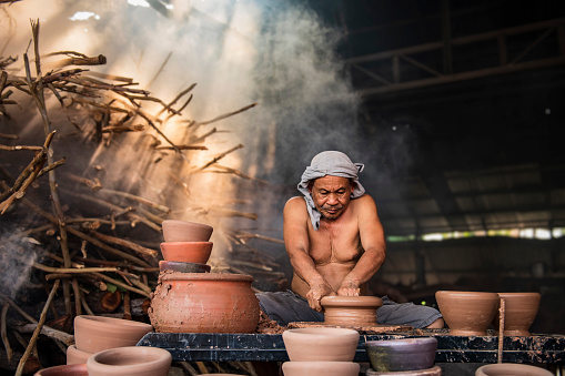 A senior man is using a potter's wheel to make pottery from wet clay.