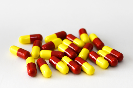 Close up view of unmarked red and yellow gelatin capsules containing drugs on a plain white background. No people.