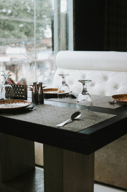 istock Window Illuminated Restaurant table with cluttered plates & Flipped wine glasses 1421957422