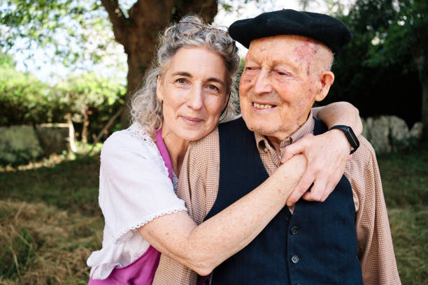 cariñoso abrazo de una hija a su padre de noventa y seis años mientras ambos sonríen a cámara. - retirement grandfather senior adult child fotografías e imágenes de stock