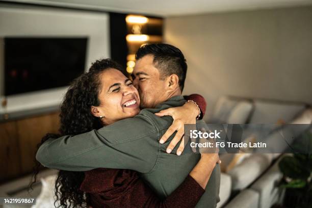 Mid Adult Couple Embracing In The Living Room At Home Stock Photo - Download Image Now
