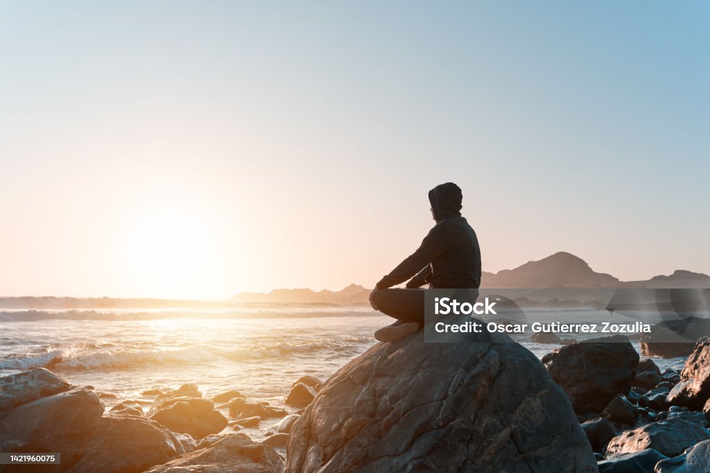 silhouette of a person sitting meditating on the rock on the coast at sunset Mindfulness Stock Photo