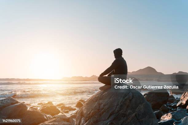 Silhouette Of A Person Sitting Meditating On The Rock On The Coast At Sunset Stock Photo - Download Image Now