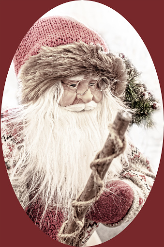 Old fashioned woodland Christmas Santa with knit fir trimmed hat and spectacles holding walking stick - Vintage filter with oval frame and dark red background - focus on face