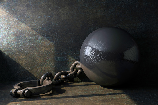 leg shackles with a ball illuminated by a beam of light in a dungeon. 3d rendering