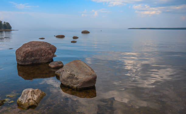 Boulders in the sea and clouds reflecting back on the still water by the rocky Baltic coastal shoreline in Käsmu, Estonia. stock photo