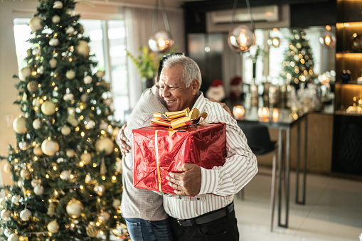 Senior man embracing his grandson after receiving christmas present on christmas at home