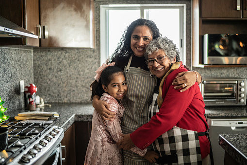 Abuela, madre e hija abrazadas en la cocina de casa photo