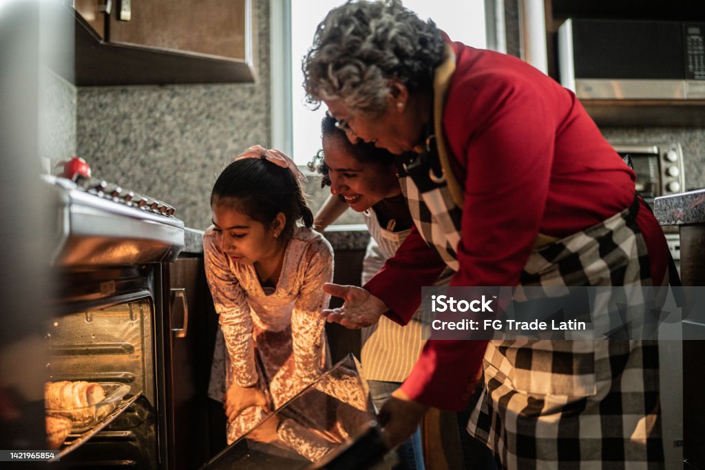 Grandmother, mother and daughter looking at food in the oven at home Family Stock Photo