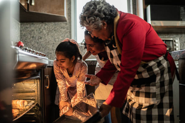 Grandmother, mother and daughter looking at food in the oven at home stock photo