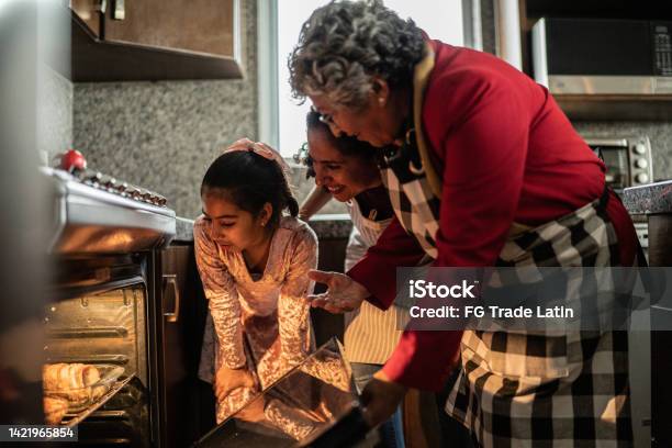 Grandmother Mother And Daughter Looking At Food In The Oven At Home Stock Photo - Download Image Now
