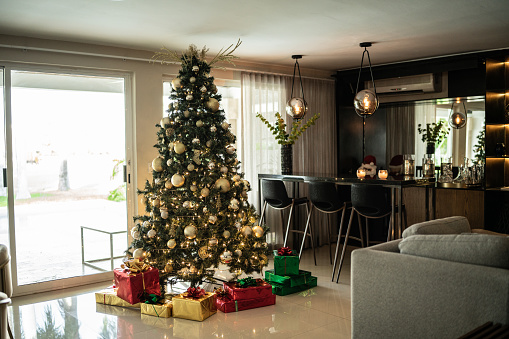 Decorated Christmas tree with gifts underneath. Wide angle photo with whole cosy living room visible. Christmas morning. No people. Daylight.