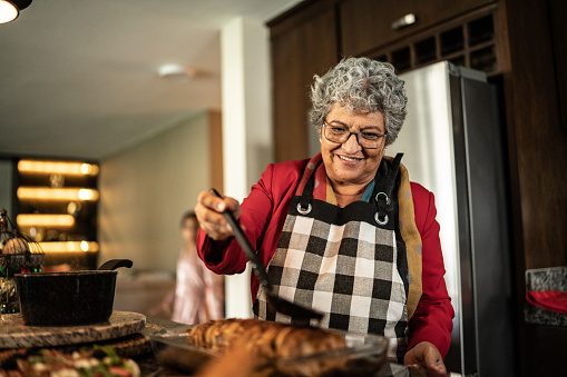 Mujer mayor poniendo salsa en lomo con fruta en la encimera de la cocina en casa photo