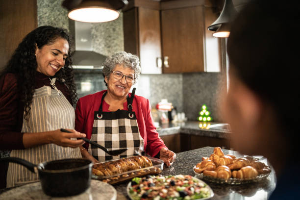 Mother and daughter talking while preparing food at kitchen counter at home stock photo