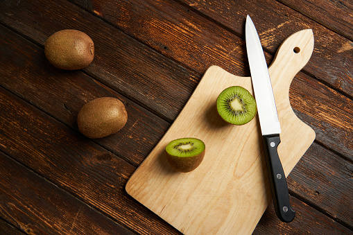 One kiwi fruit cut in halves and two whole kiwi fruit with a knife on wooden table and background.