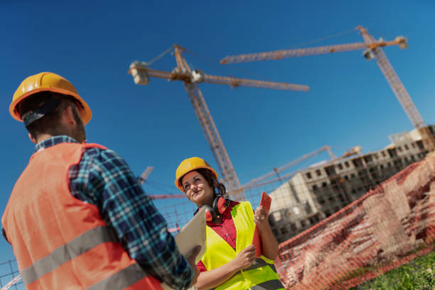 istock Workers on construction site with construction cranes / towers high above. 1421973097