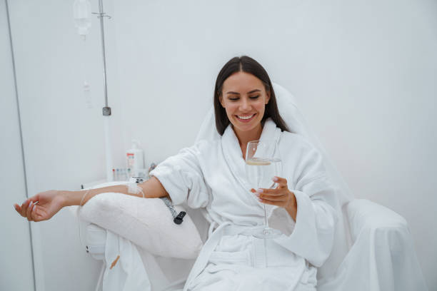 piękna kobieta w białym szlafroku pije wodę podczas zabiegu medycznego w gabinecie kosmetycznym - iv drip zdjęcia i obrazy z banku zdjęć