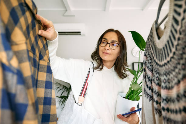 glückliche frau, die neue kleidung im laden kauft. gestrickte pullover an kleiderbügeln am kleiderständer. slow fashion.bewusster konsum. garagenverkauf, wiederverwendung von kleidung, second hand und öko-consumering-konzept - autumn women clothing retail stock-fotos und bilder