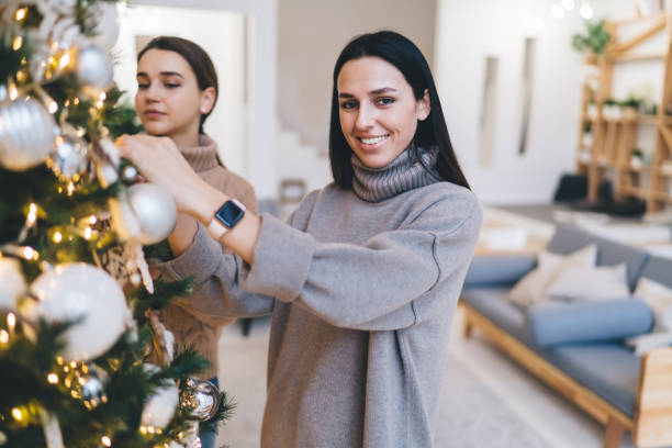 istock Smiling woman decorating Christmas tree with friend 1421979054