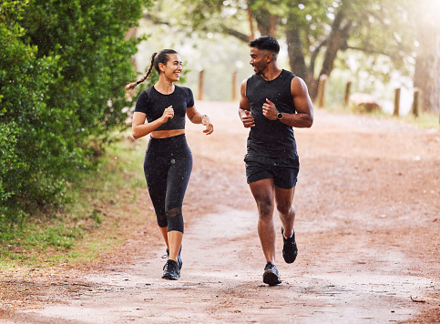 Fitness, exercise and happy couple out running or jogging on a forest trail or park outdoors. Sporty and smiling man and woman staying active and fit while exercising and bonding during a workout