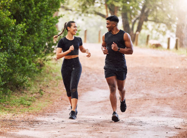 fitness, exercise and happy couple out running or jogging on a forest trail or park outdoors. sporty and smiling man and woman staying active and fit while exercising and bonding during a workout - wood dirt road footpath exercising imagens e fotografias de stock