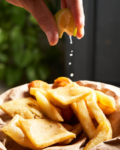 Close-up of unrecognizable man squeezing a lemon smoothly over french fries.