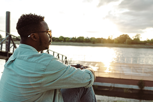 Young African American man sitting by the river and looking at the distance