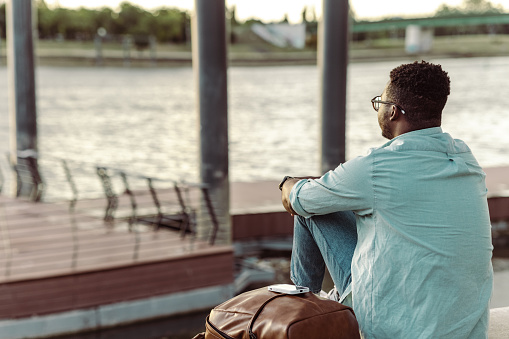 Young African American man sitting by the river and looking at the distance