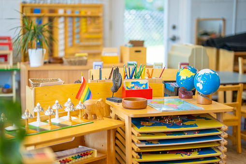 A Montessori classroom set-up complete with desks, paint racks, globes, musical instruments, plants, writing utensils, and other education inspiring tools.