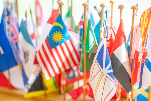 A large assortment of colorful country flags are seen standing up on a desk in a Montessori classroom.