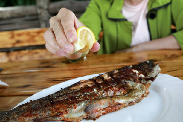 Person squeezes juice from lemon on grilled trout in restaurant