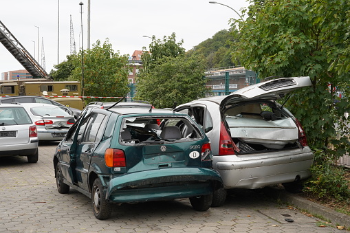 Hamburg, Germany 08 27 2022: Smashed and wrecked cars of green and silver color on the parking lot in Germany near bushes and other vegetation.