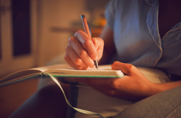 scrittura creativa a casa da mani femminili che si godono una giornata calma e pacifica al chiuso. donna che prende appunti in un diario, esprimendo i suoi sentimenti e pensieri mentre prende nota di un'esperienza personale - diary writing women human hand foto e immagini stock