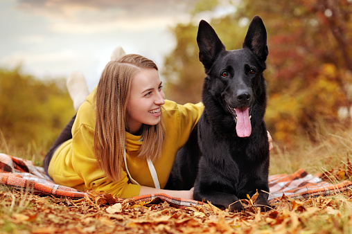 Woman with her shepherd dog laying on the plaid in the autumn forest