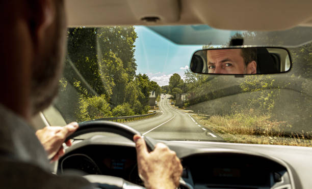 Caucasian man driving a car. View of the countryside road from the windshield of the vehicle. Caucasian man driving a car. View of the countryside road from the windshield (front window) of the vehicle. Face reflection in the rear-view mirror. hit the road stock pictures, royalty-free photos & images
